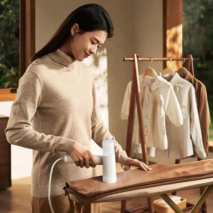 Défroisseur vapeur à main blanc défroissant une chemise sur un cintre